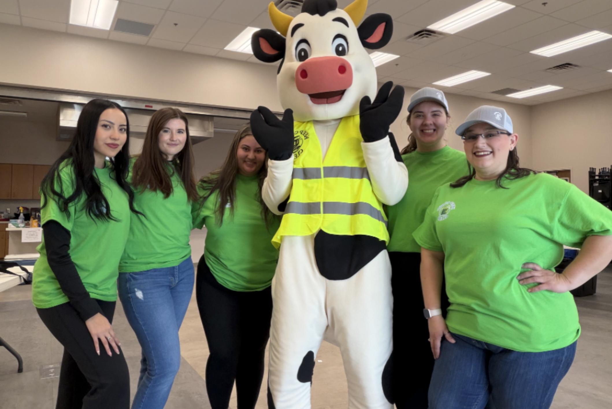 A costume cow with their hands in the air surrounded by 5 volunteers.
